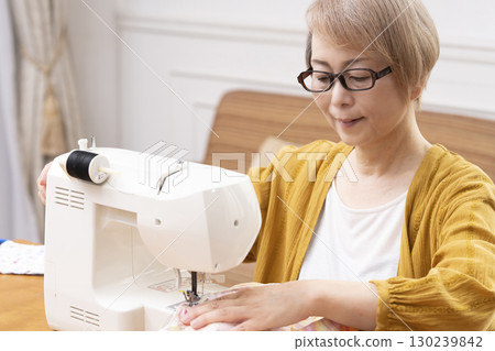 一位老年婦女高興地用縫紉機縫製衣服和配件 130239842