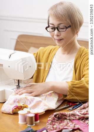 A senior woman happily sewing clothes and accessories with a sewing machine 130239843