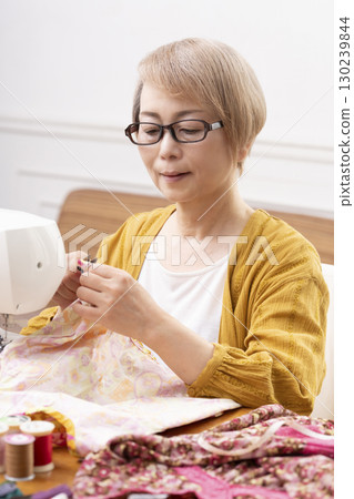 A senior woman happily sewing clothes and accessories with a sewing machine 130239844