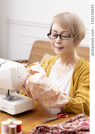 A senior woman happily sewing clothes and accessories with a sewing machine A senior woman happily sewing clothes and accessories with a sewing machine 130239845
