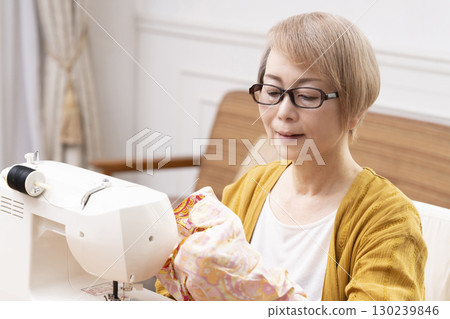 一位老年婦女高興地用縫紉機縫製衣服和配件 一位老年婦女高興地用縫紉機縫製衣服和配件 130239846