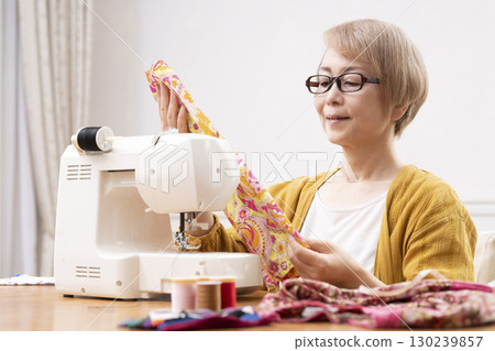 A senior woman happily sewing clothes and accessories with a sewing machine 130239857