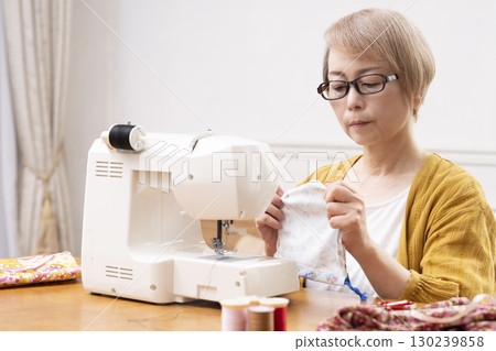 一位老年婦女高興地用縫紉機縫製衣服和配件 130239858