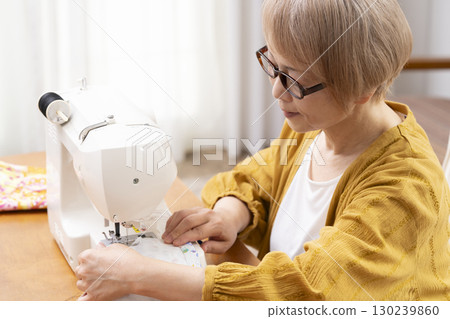A senior woman happily sewing clothes and accessories with a sewing machine A senior woman happily sewing clothes and accessories with a sewing machine 130239860