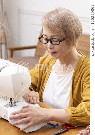 一位老年婦女高興地用縫紉機縫製衣服和配件 一位老年婦女高興地用縫紉機縫製衣服和配件 130239862
