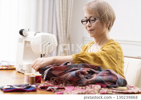 一位老年婦女高興地用縫紉機縫製衣服和配件 130239868