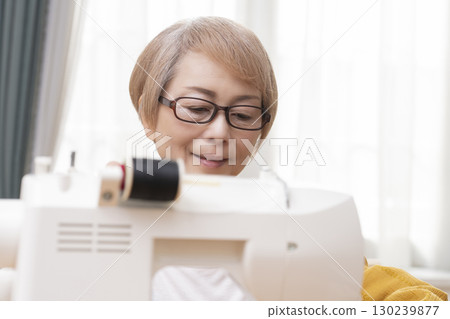 一位老年婦女高興地用縫紉機縫製衣服和配件 130239877