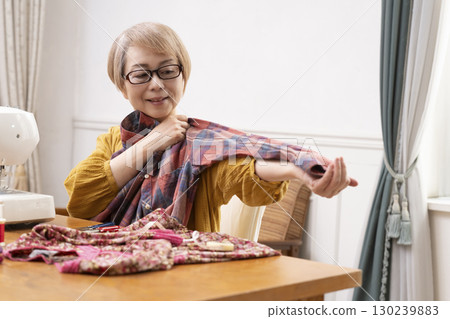 一位老年婦女高興地用縫紉機縫製衣服和配件 一位老年婦女高興地用縫紉機縫製衣服和配件 130239883