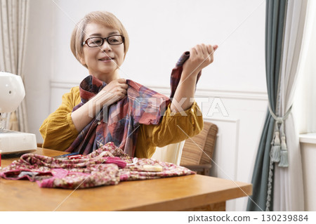 一位老年婦女高興地用縫紉機縫製衣服和配件 130239884
