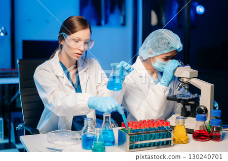 Young scientists conducting research investigations in a medical laboratory, a researcher in the foreground is using a microscope in laboratory 130240701
