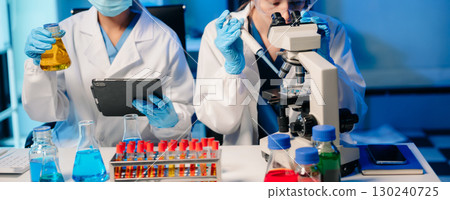 Modern Medical Research Laboratory Portrait of Two Scientists Working, Using Digital Tablet, Analyzing Samples, Talking. 130240725