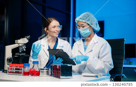 Modern Medical Research Laboratory Portrait of Two Scientists Working, Using Digital Tablet, Analyzing Samples, Talking. 130240785