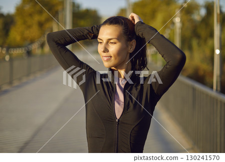 Portrait of a happy active sporty young woman standing in the park after fit training. 130241570