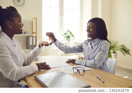 Happy, smiling African American woman real estate agent gives house keys to client 130241679