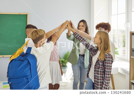 Happy school children with teacher standing in the classroom with hands in stack together. 130241680