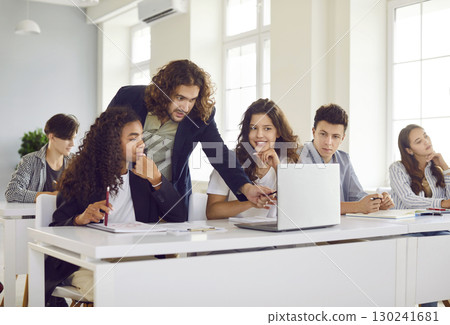 Group of classmates sitting in classroom with male teacher and looking at laptop monitor screen. 130241681