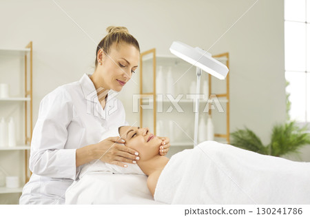 Young female cosmetologist examining woman client skin condition in beauty salon. 130241786
