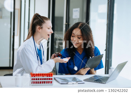 Doctor Talks With Professional Head Nurse or Surgeon, They Use Digital tablet Computer. Diverse Team of Health Care Specialists Discussing Test Result 130242202