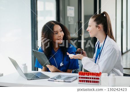 Doctor Talks With Professional Head Nurse or Surgeon, They Use Digital tablet Computer. Diverse Team of Health Care Specialists Discussing Test Result 130242423