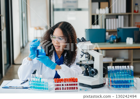 Young scientists conducting research investigations in a medical laboratory, a researcher in the foreground is using a microscope Young scientists conducting research investigations in a medical laboratory, a researcher in the foreground is using a microscope 130242494