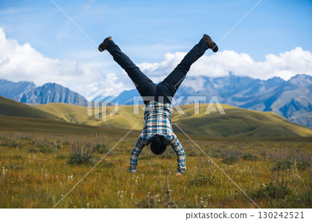 Woman hiker doing a handstand on high altitude mountain top grassland Woman hiker doing a handstand on high altitude mountain top grassland 130242521