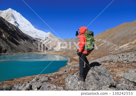 Backpacking woman taking photo with smartphone on high altitude mountain top Backpacking woman taking photo with smartphone on high altitude mountain top 130242553