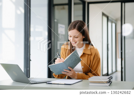 Confident woman with a smile standing holding notepad and tablet at the office. Confident woman with a smile standing holding notepad and tablet at the office. 130242682