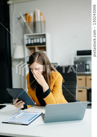 Woman who is tired and overthinking from working with tablet and laptop Woman who is tired and overthinking from working with tablet and laptop 130243006