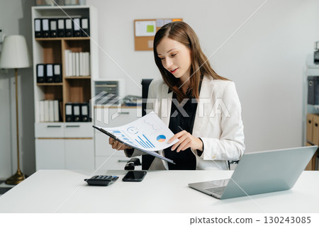 Confident business expert attractive smiling young woman typing laptop and holding digital tablet Confident business expert attractive smiling young woman typing laptop and holding digital tablet 130243085