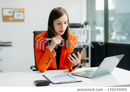 Confident business expert attractive smiling young woman typing laptop and holding digital tablet 130243093