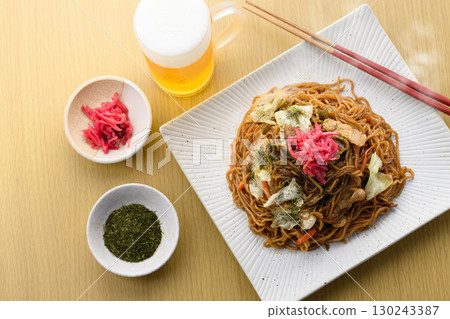 新鮮出爐的熱騰騰的炒麵配上醬汁和冰鎮啤酒——這是經典的居酒屋菜單,配有飲料。 新鮮出爐的熱騰騰的炒麵配上醬汁和冰鎮啤酒——這是經典的居酒屋菜單,配有飲料。 130243387