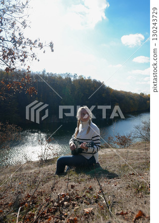 Portrait of smiling caucasian girl plays ukulele in autumnal park. Young woman plays guitar musical instrument outside in nature fall time. Audio music healing 130243729