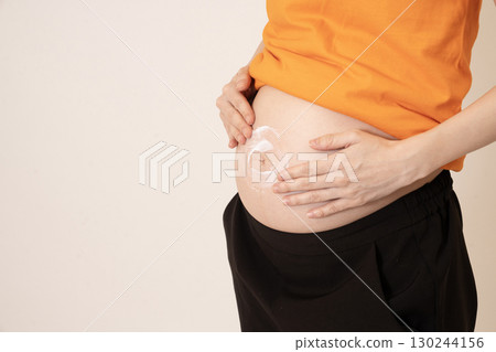 Woman applying cream to her 8-month pregnant belly 130244156