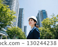 a japanese female engineer wearing a blue suit and holding a white helmet stands in front of tall office buildings 130244238