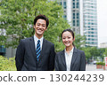 young japanese business people, a man and a woman, in office attire, standing in front of an office building 130244239