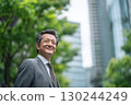 a japanese businessman in a suit is smiling while standing outdoors near green trees and buildings 130244249