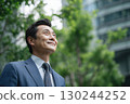 a japanese businessman stands in front of an office building, smiling and gazing at the sky 130244252