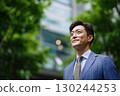 a japanese businessman, wearing a suit with a tie, stands in front of an office building 130244253