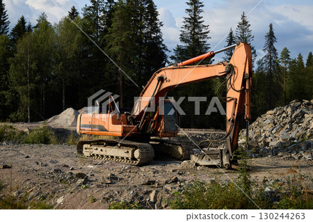 An Excavator is Actively Working on a Construction Site that is Surrounded by Lush Nature 130244263