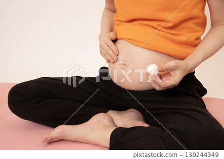 Woman applying cream to her 8-month pregnant belly Woman applying cream to her 8-month pregnant belly 130244349