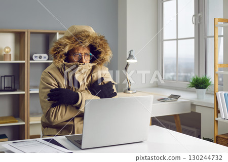 Young african american man working in the cold at home on his laptop computer trying to keep warm. 130244732