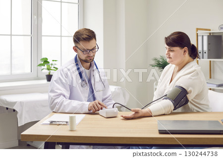 Doctor uses sphygmomanometer to check blood pressure of young overweight woman patient Doctor uses sphygmomanometer to check blood pressure of young overweight woman patient 130244738
