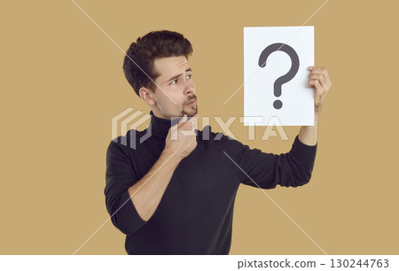 Pensive man is looking at piece of paper with question mark drawn on it, which he is holding in hand 130244763