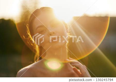 Young woman enjoying a sunset, with soft light illuminating her face and a dreamy expression, ideal for serene lifestyle concepts and summer themes 130245794