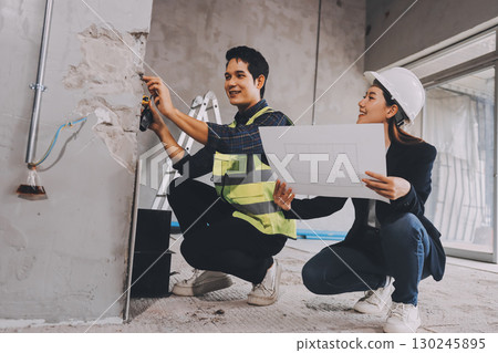 Construction manager and engineer dressed in orange work vests and hard helmets explore construction documentation on the building site near the steel frames 130245895