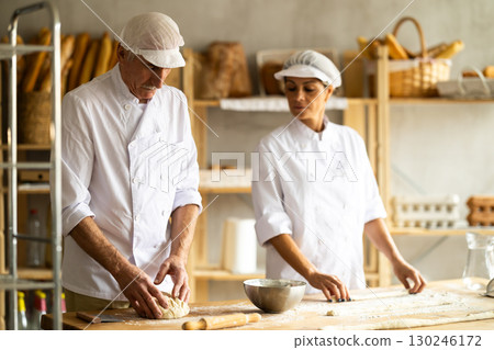 Elderly male chef and female skillfully kneads dough to bake delicious bread and croissants Elderly male chef and female skillfully kneads dough to bake delicious bread and croissants 130246172