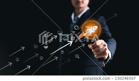Businesswoman pointing at startup rocket icon with digital arrows, symbolizing innovation, growth, technology, entrepreneurship, success, leadership and future business development. 130246507