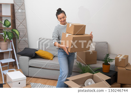 A content and delighted woman moves to her new home, standing in the living room with a pile of cardboard relocation boxes, feeling at home A content and delighted woman moves to her new home, standing in the living room with a pile of cardboard relocation boxes, feeling at home 130246744