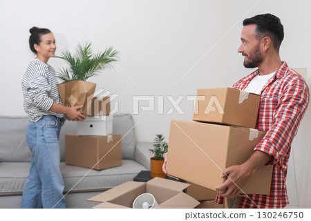 New Living Space: A satisfied young couple stands in their new home's living room, surrounded by a heap of cardboard boxes from their international relocation, making their space their own 130246750