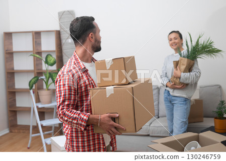 Young friends, elated and satisfied, enters their new home's living room with a heap of cardboard boxes from their international move, marking a fresh start 130246759